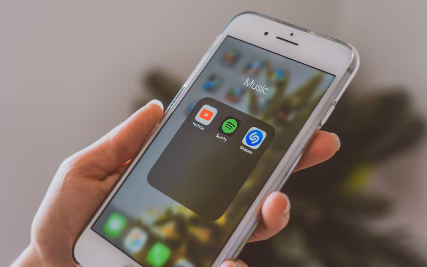 A hand holds a smartphone showing YouTube, Spotify and Shazam music apps.