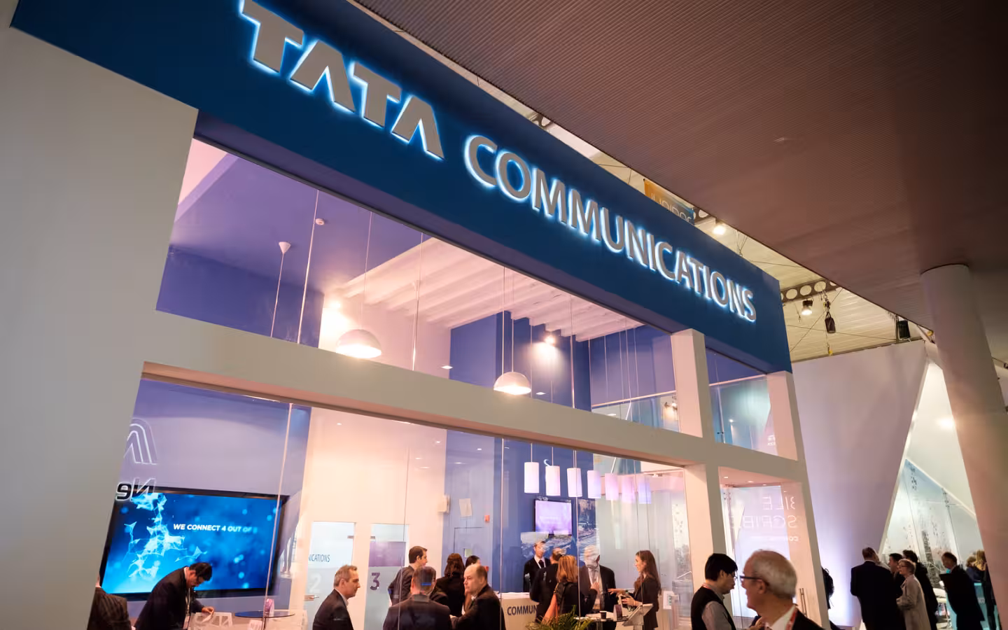 Tata Communications exhibition booth with an illuminated sign and visitors below
