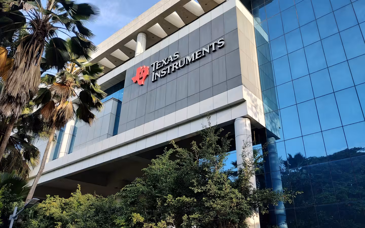 Texas Instruments sign on a glass-fronted Bagmane Tech Park building amid palms