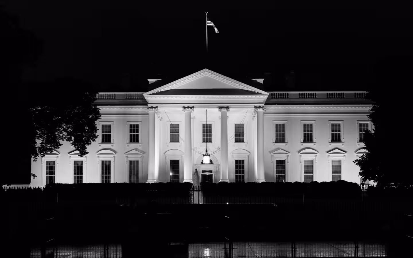 The White House illuminated at night, with a flag above its roof.
