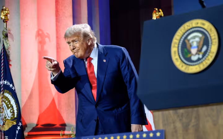 President Donald Trump points onstage beside a presidential seal and flag.