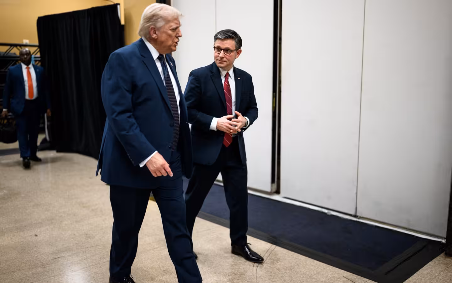 Donald Trump walks beside Mike Johnson through an indoor hallway.