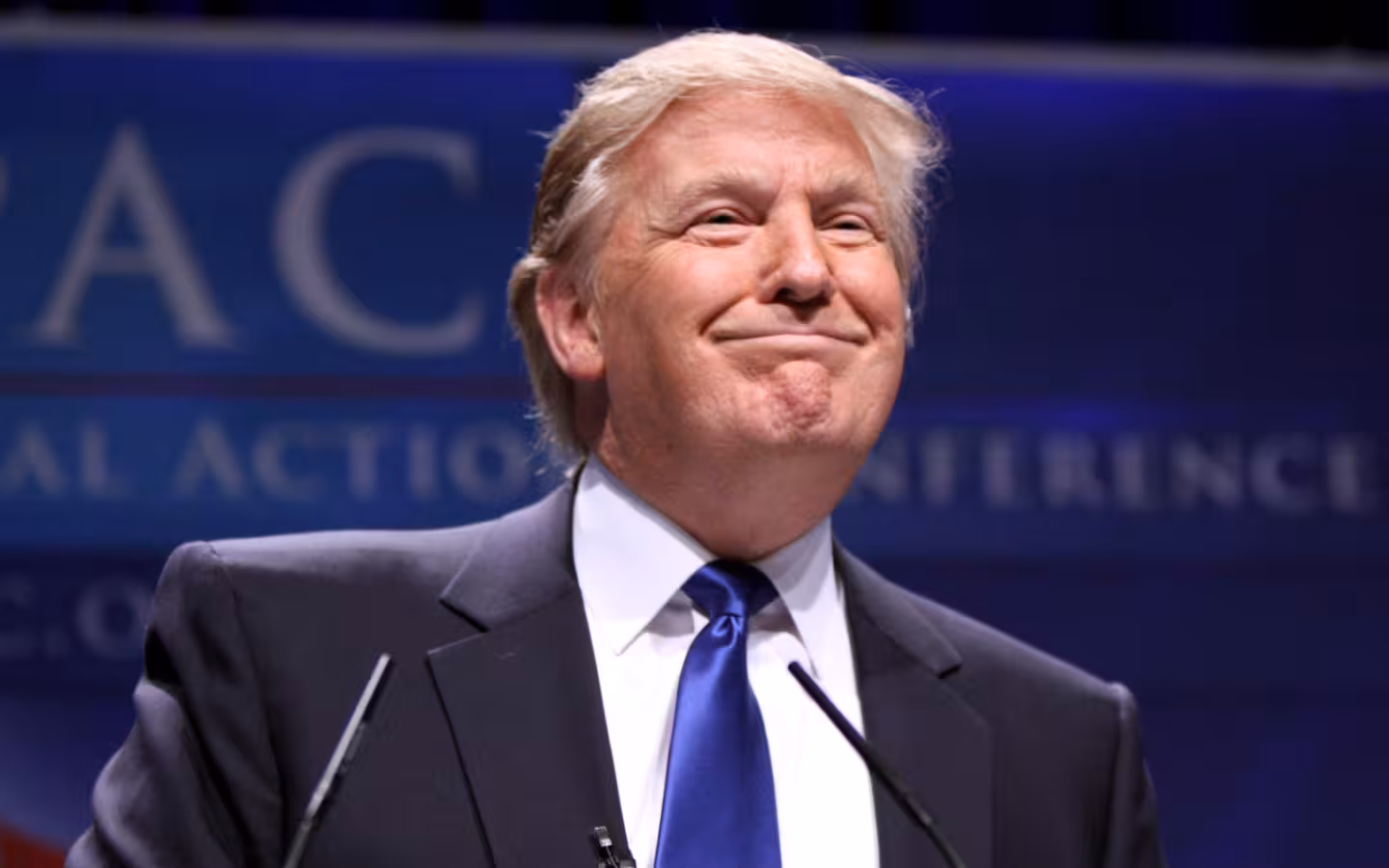 Donald Trump speaking at a lectern before a blurred CPAC backdrop.