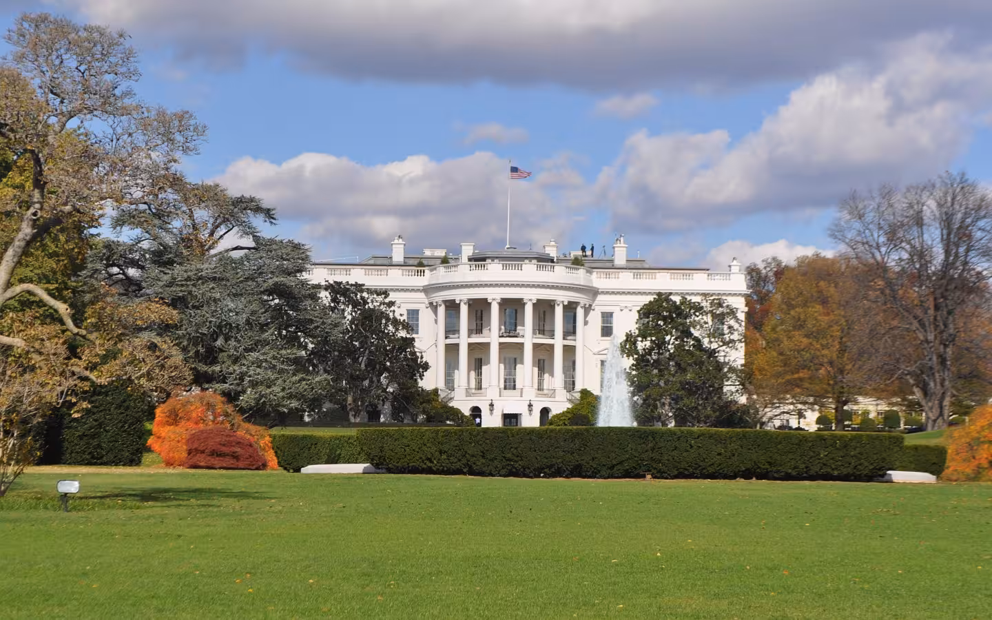 The White House beyond a broad lawn, trees and a fountain.