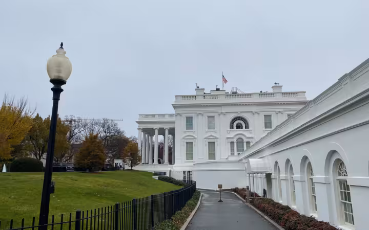 The White House West Wing beside a fenced lawn and driveway.