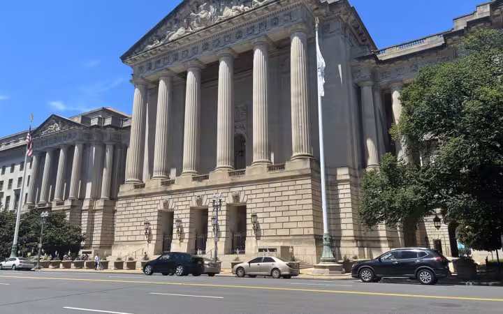 The columned facade of Andrew W. Mellon Auditorium beside a street with cars