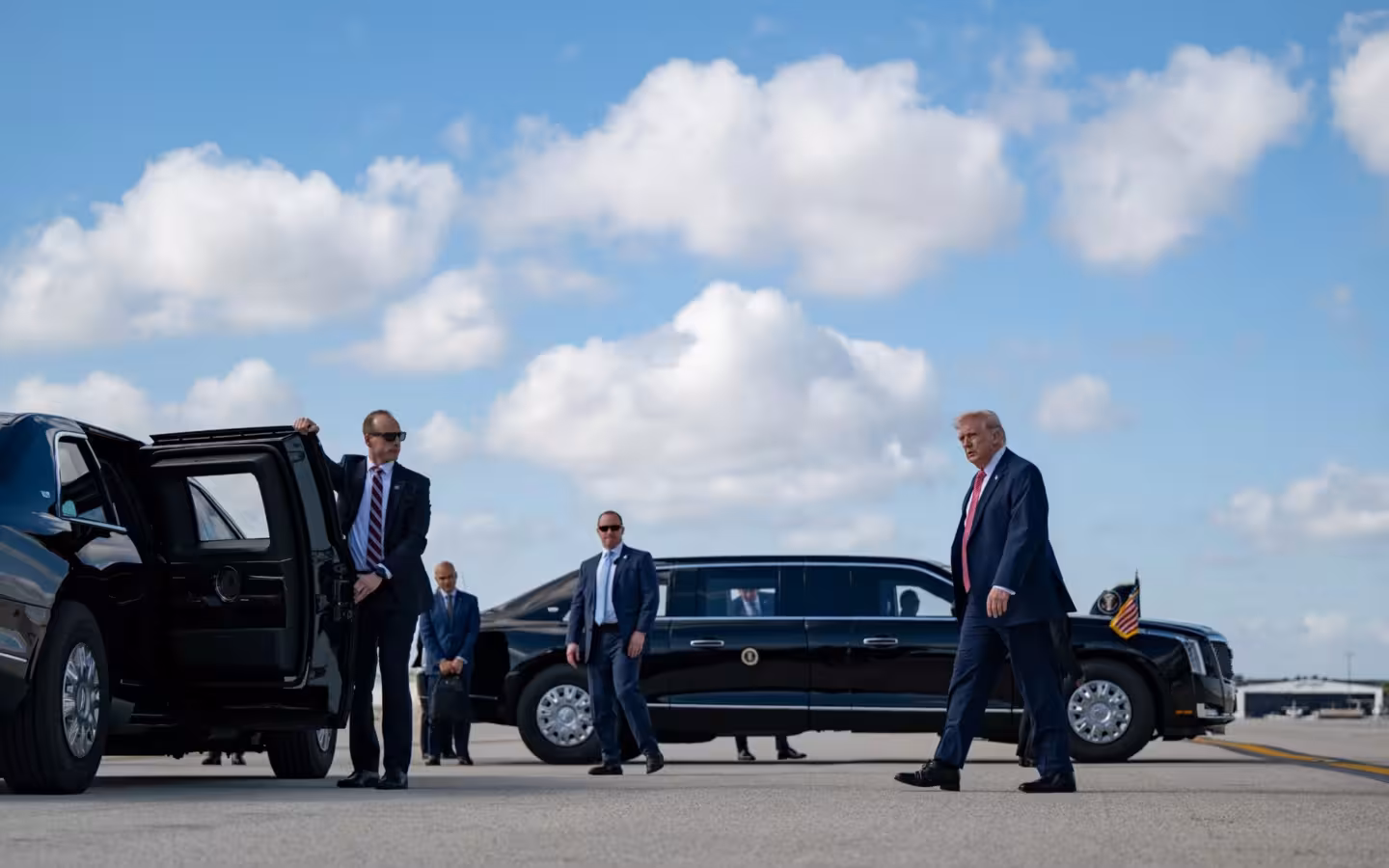 Donald Trump walks toward a motorcade with security personnel nearby.