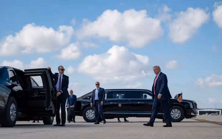 Donald Trump walks toward a motorcade with security personnel nearby.