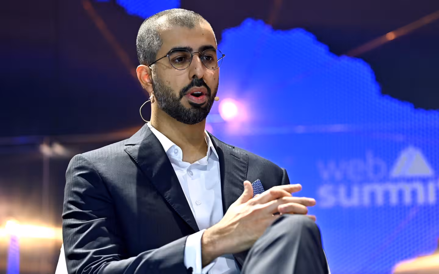 Omar Sultan Al Olama speaks onstage against a blue summit backdrop.