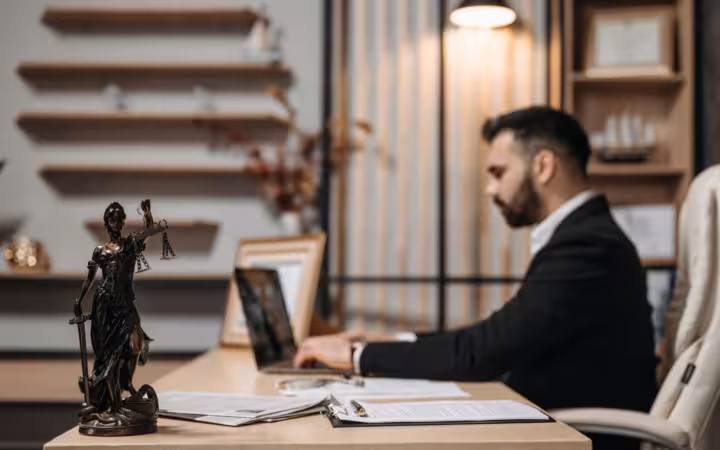 A lawyer working on a laptop at a desk with a Lady Justice statue