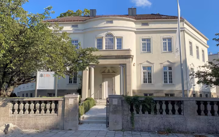 A UBS building in Munich behind a stone fence and trees