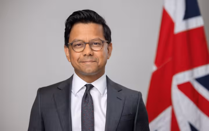 Kanishka Narayan poses in a suit beside a British flag.