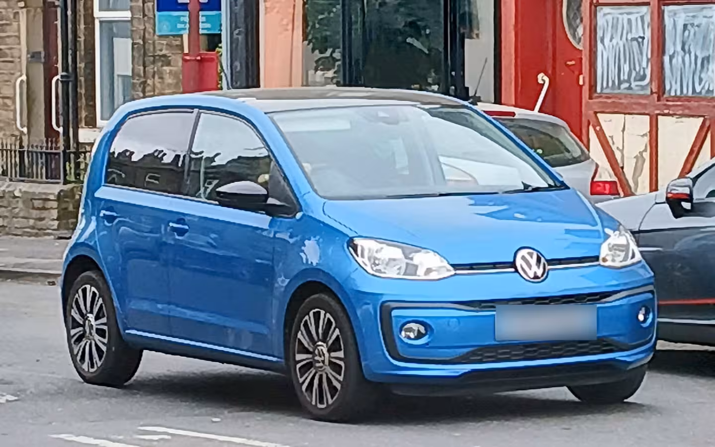 A blue Volkswagen Up parked on a street beside other cars.