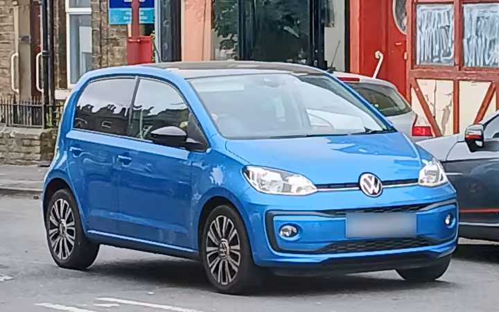 A blue Volkswagen Up parked on a street beside other cars.