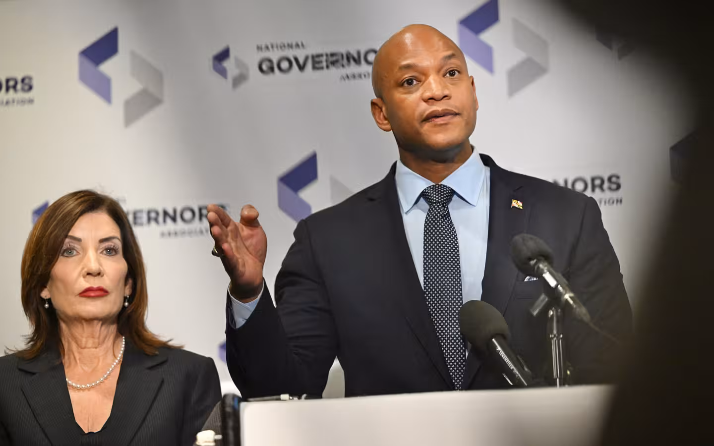 Wes Moore speaks at microphones beside another official against a governors’ backdrop.