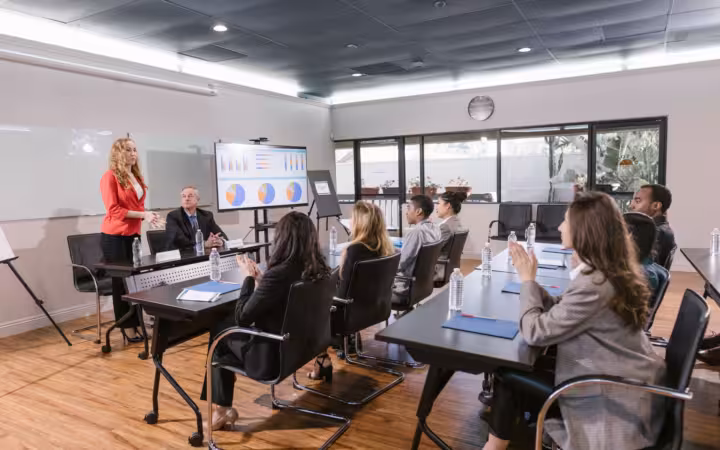 Business professionals attend a meeting around tables in a modern conference room.