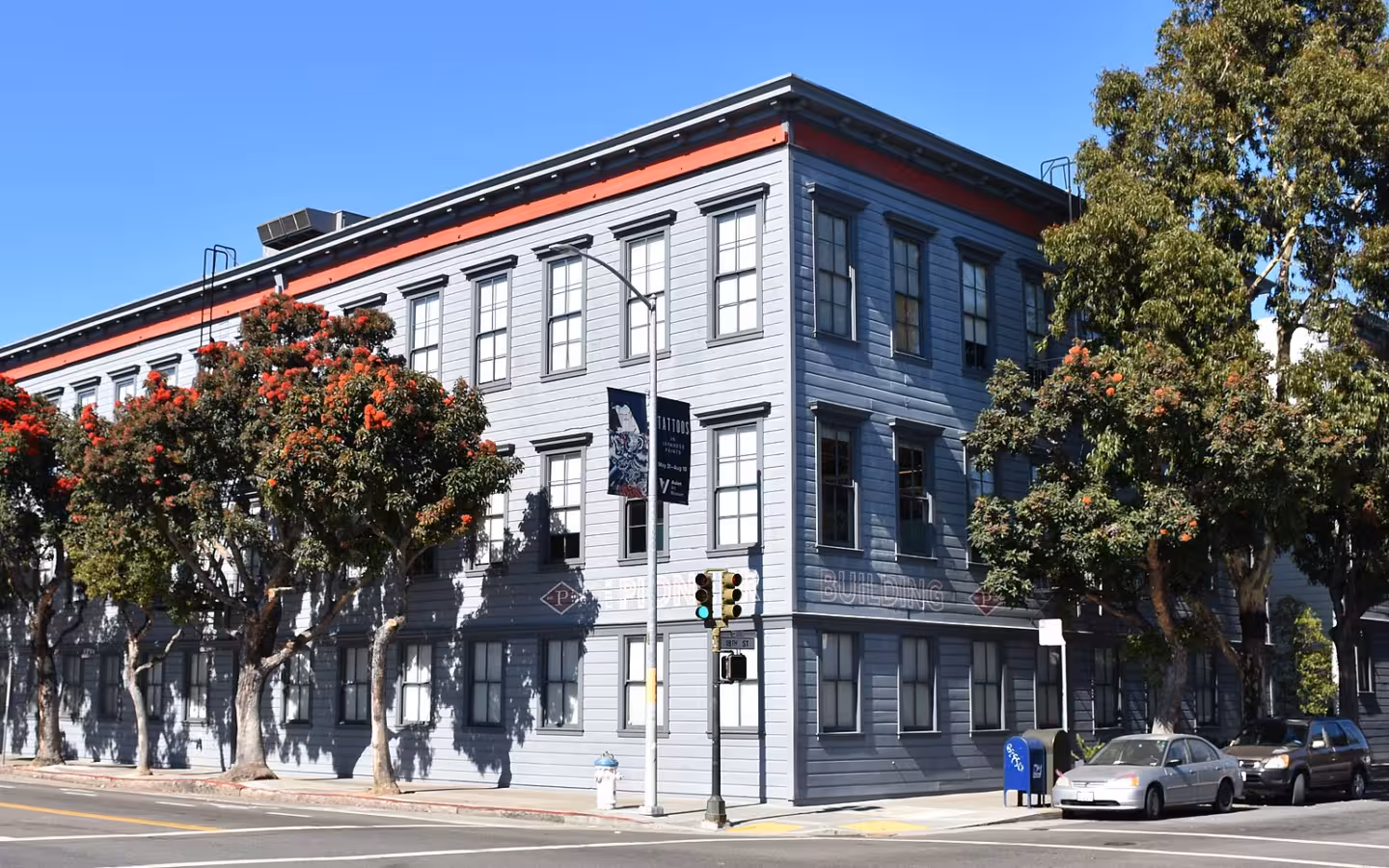 The Pioneer Building in San Francisco, partly screened by trees, beside parked cars.