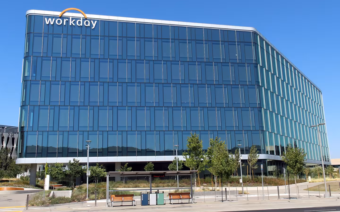 Workday headquarters, a glass office building, behind trees and benches.