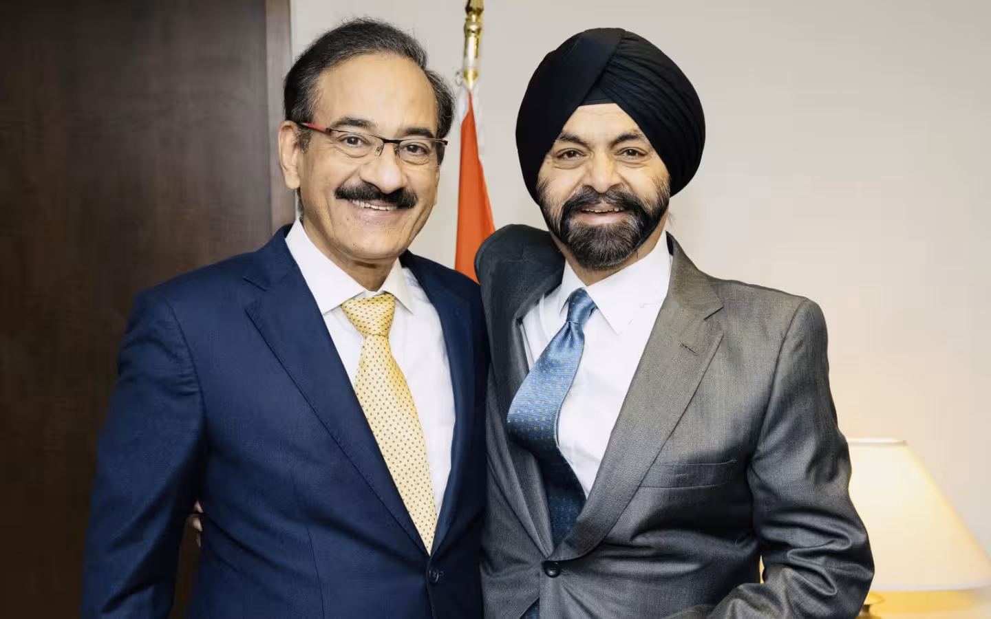Ajay Banga and Rajesh Khullar pose together in suits beside a flag.