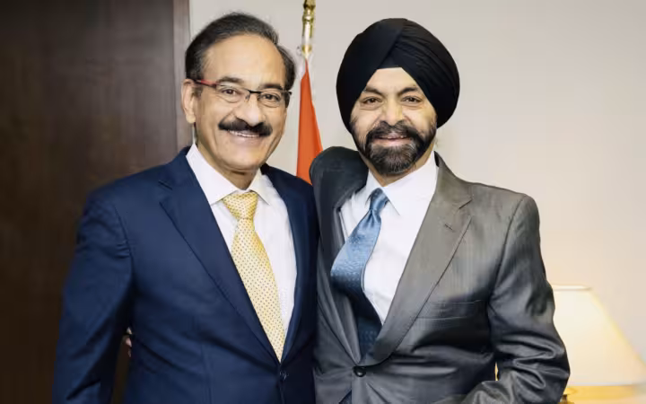 Ajay Banga and Rajesh Khullar pose together in suits beside a flag.